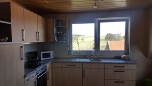 Cozinha com armários de madeira, micro-ondas, fogão e janela com vista para um campo.