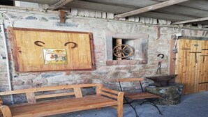 Paredão rústico de pedra com um banco de madeira, uma porta de madeira e uma roda.