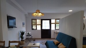 Ein Wohnzimmer mit einer Couch, einem Esstisch, Stühlen, einem Fernseher und einer Hängeleuchte.