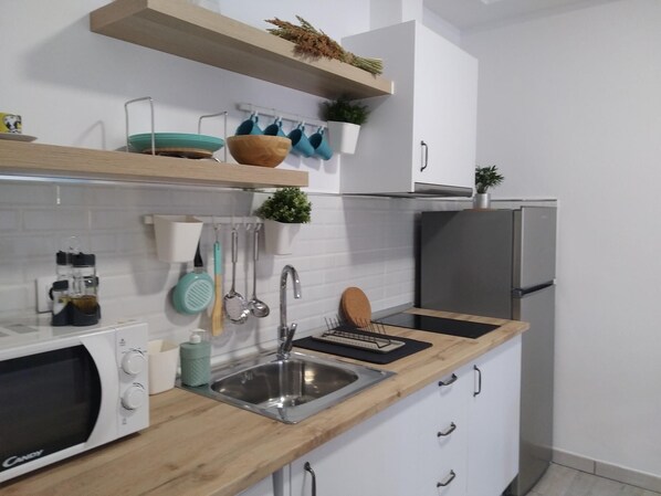 A modern kitchen with white cabinets, a wooden countertop, a stainless steel sink, and a built-in microwave.