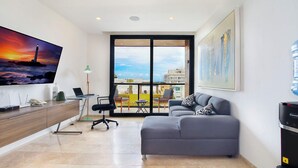 Sala de estar moderna com sofá, escrivaninha com laptop, televisão na parede e varanda com vista.