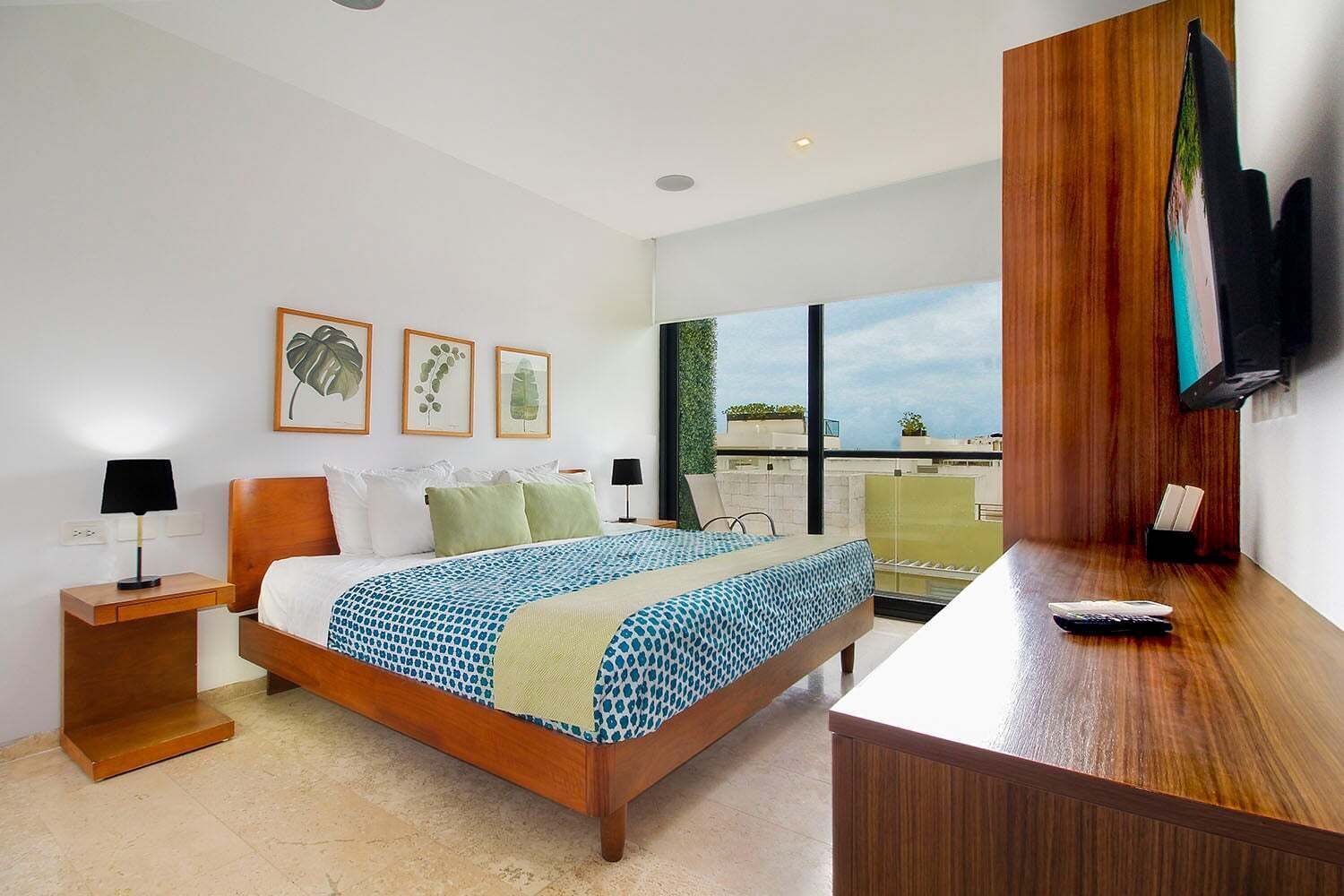 Quarto de hotel com cama, mesas de cabeceira, escrivaninha, televisão e janela com vista.