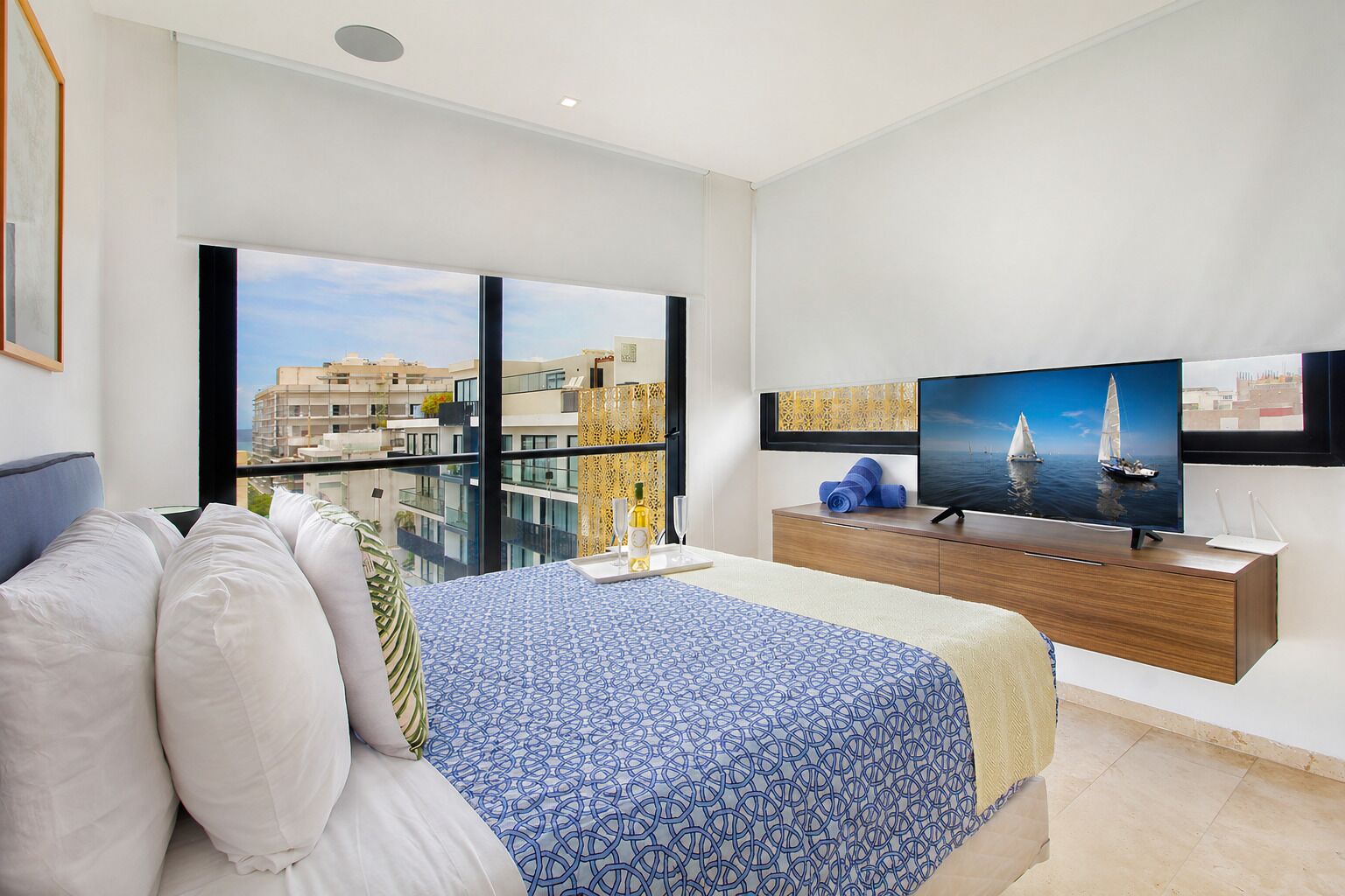 Ein Schlafzimmer mit Bett, Fernseher, Fenster und Balkon mit Blick auf die Stadt.