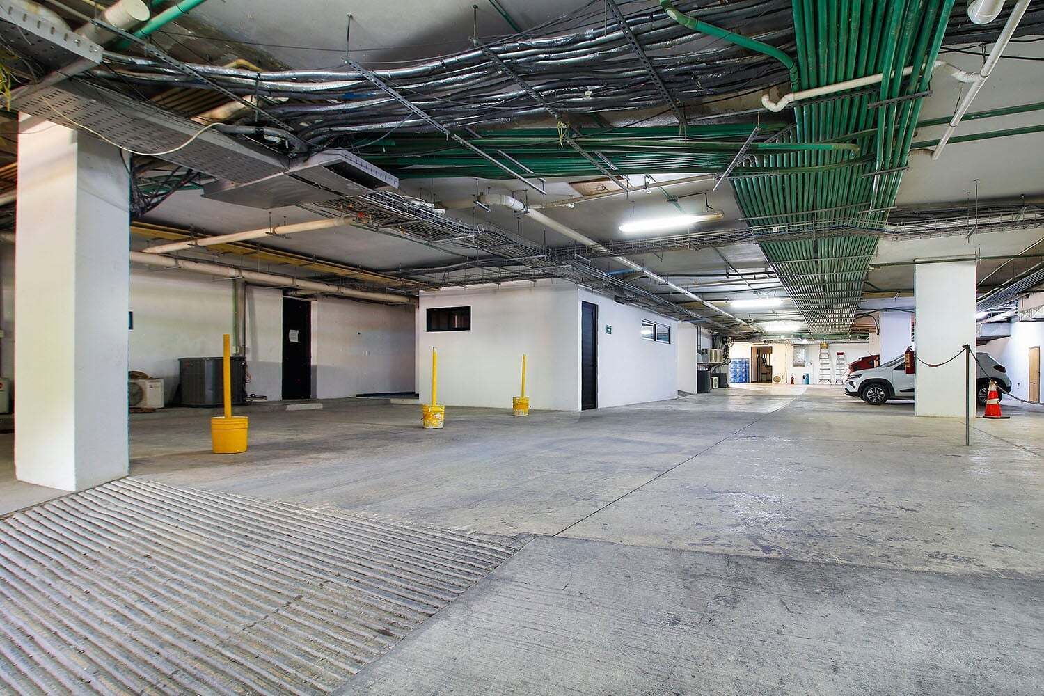 Un parking intérieur avec des planchers en béton, des murs verts et blancs, et des tuyaux apparents au plafond.