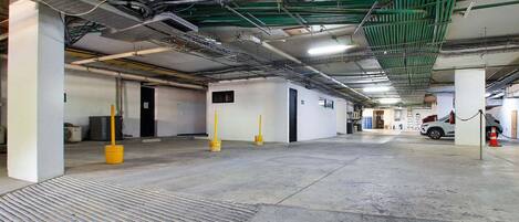 Un parking intérieur avec des planchers en béton, des murs verts et blancs, et des tuyaux apparents au plafond.