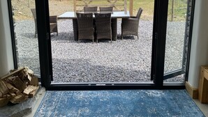 Ein Zimmer mit einer großen Glasdoor, die zu einem Außenbereich mit Korbmöbeln und Blick auf eine grüne Landschaft führt.