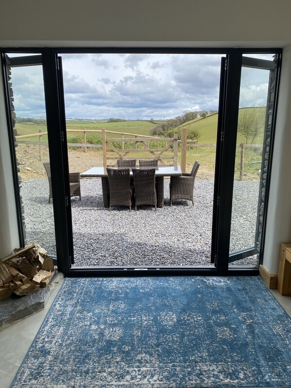 A room with a large glass door leading to an outdoor seating area with wicker furniture and a view of a green landscape.
