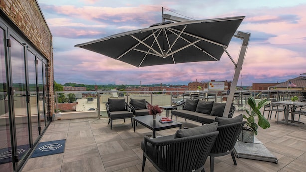 A rooftop patio with outdoor furniture, a large umbrella, and a view of the cityscape.