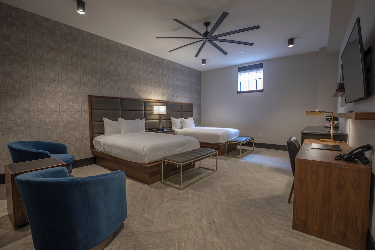A modern hotel room with a large bed, two smaller beds, a desk, and a chair.