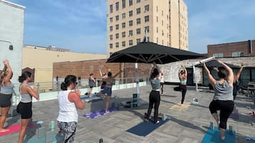 Um grupo de pessoas praticando yoga em tapetes ao ar livre em ambiente urbano, com edifícios ao fundo.