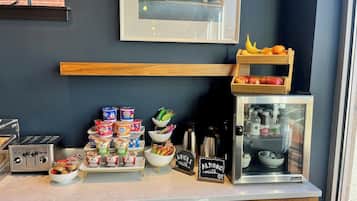 A breakfast bar with various food items, a refrigerator with milk, and a wooden shelf with fruits.