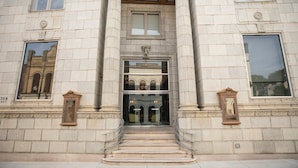 A building entrance with a grand staircase, large windows, and decorative moldings.