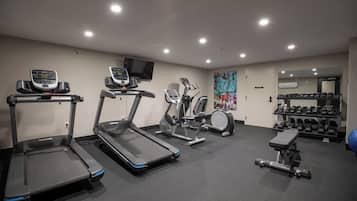 Ein Fitnessraum mit Laufbändern, Crosstrainern, Kurzhanteln und einer Trainingsbank.