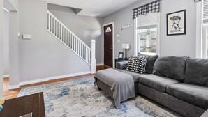 A living room with a gray sofa, patterned rug, and a staircase leading to another room.