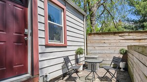 A patio with two chairs and a table, a red door, and a window with a red frame.