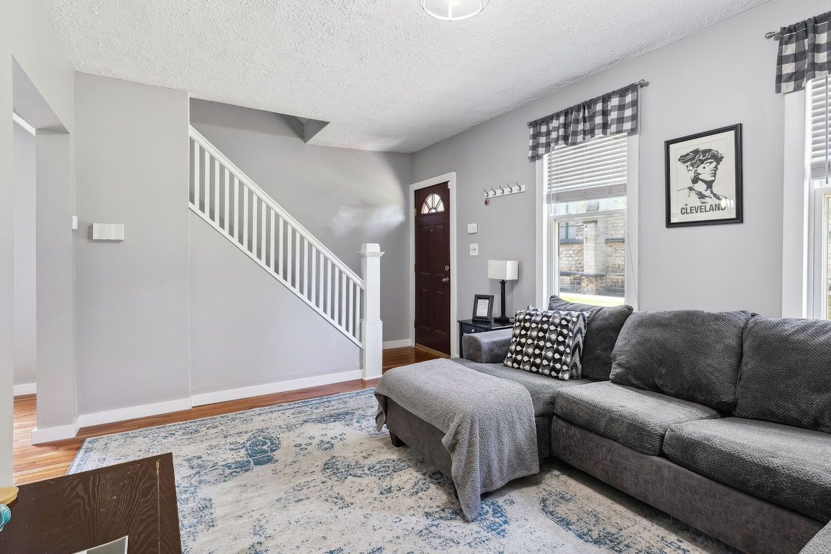 A living room with a gray sofa, a patterned rug, a staircase, and a door with a window.