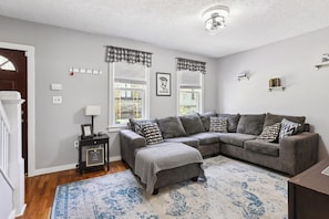 A living room with a grey sectional sofa, a patterned rug, and a small side table with a lamp.