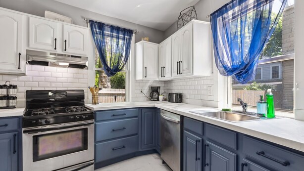 A modern kitchen with white cabinets, a stainless steel stove, and blue curtains.