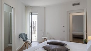 Een slaapkamer met een bed, twee kussens, een stoel en een deur naar een balkon.