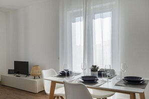 A dining area with a table set for two, a laptop on a stand, and a television on a cabinet. - Deluxe Apartment - Avio by Wonderful Italy (Genova)