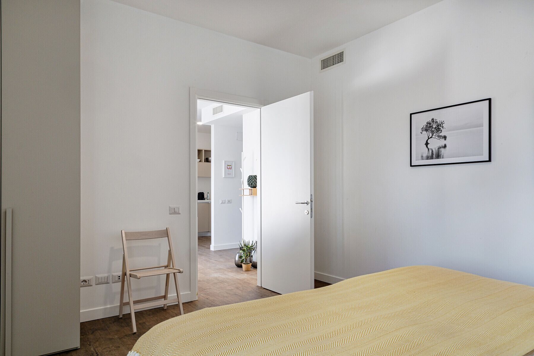 A bedroom with a bed, a chair, a door leading to a bathroom, and a framed picture on the wall.