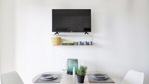 A dining area with a round table, two chairs, a television mounted on the wall, a shelf with books and cups, and a small potted plant. - Deluxe Apartment - Ice by Wonderful Italy (Genova)