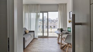A modern living room with a sofa, a dining table with chairs, and a city view through large windows. - Deluxe Apartment - Ice by Wonderful Italy (Genova)