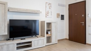 Un salon équipé d’un téléviseur à écran plat, d’un meuble de rangement en bois, d’une porte et d’une horloge murale.