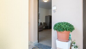 Une porte qui donne sur un espace de vie comprenant une plante en pot, un réfrigérateur et un canapé.