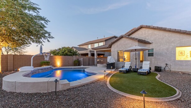 Un patio trasero con piscina, un porche techado y un césped cuidado.