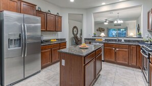 Una cocina moderna con armarios de madera, un refrigerador de acero inoxidable, encimeras de granito y una isla central.