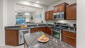 Una cocina moderna con encimeras de granito, electrodomésticos de acero inoxidable, armarios de madera y una isla central con un frutero.