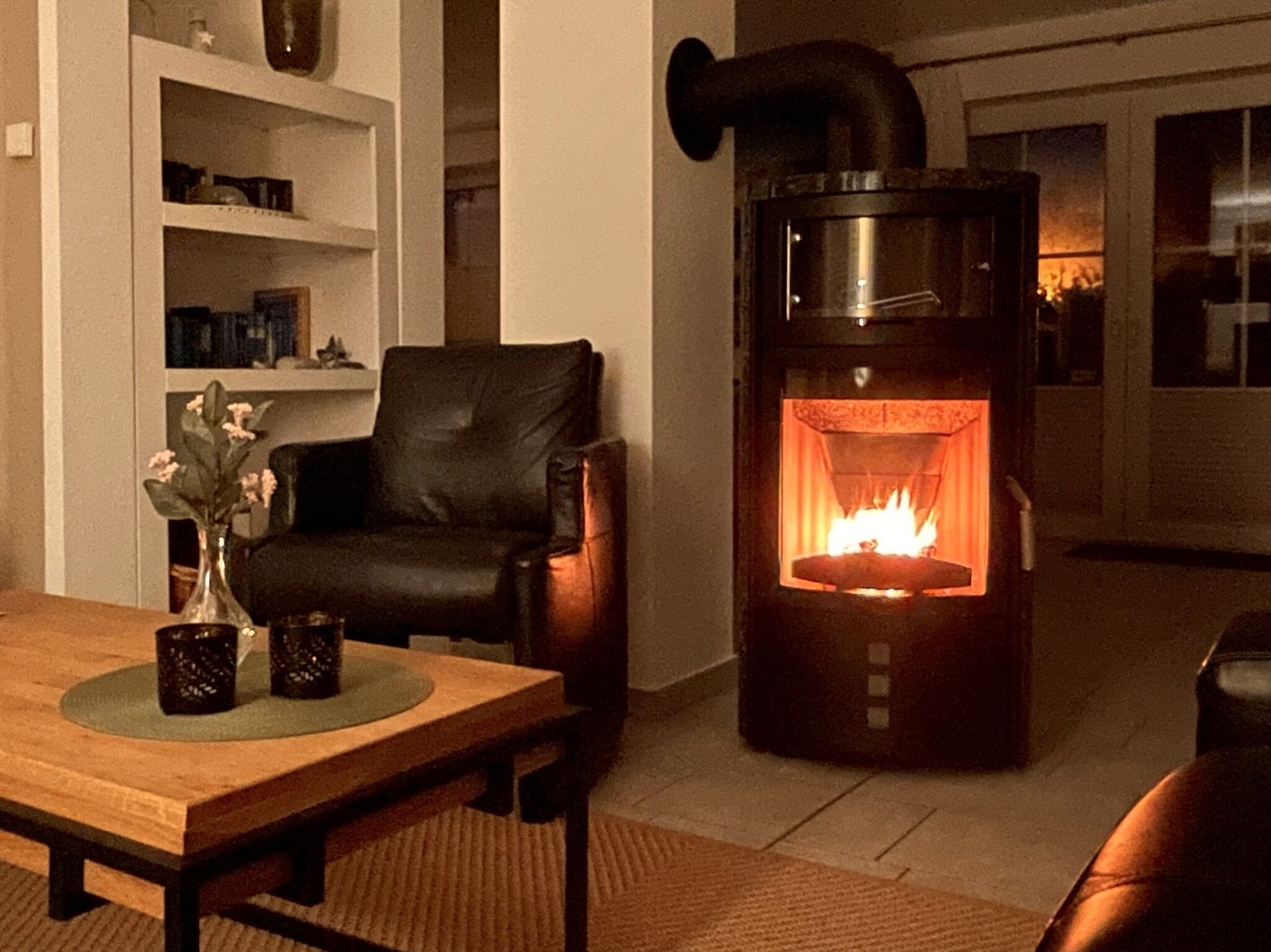 A cozy living room with a fireplace, a leather armchair, a wooden coffee table, and a bookshelf.