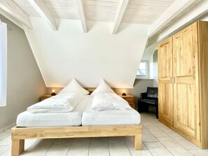 Un dormitori amb sostre d'estil loft, un llit amb estructura de fusta, dues taules de nit amb làmpades i un armari de fusta.