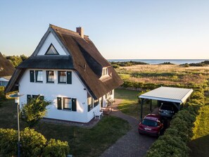 Una casa blanca amb teulada de palla, un garatge cobert i vistes al mar.
