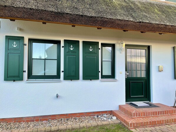 Een gebouw met een witte gevel, groene luiken en een stenen entree.