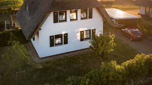 Une maison blanche avec un toit à forte pente, de nombreuses fenêtres et un garage dans lequel une voiture est garée.