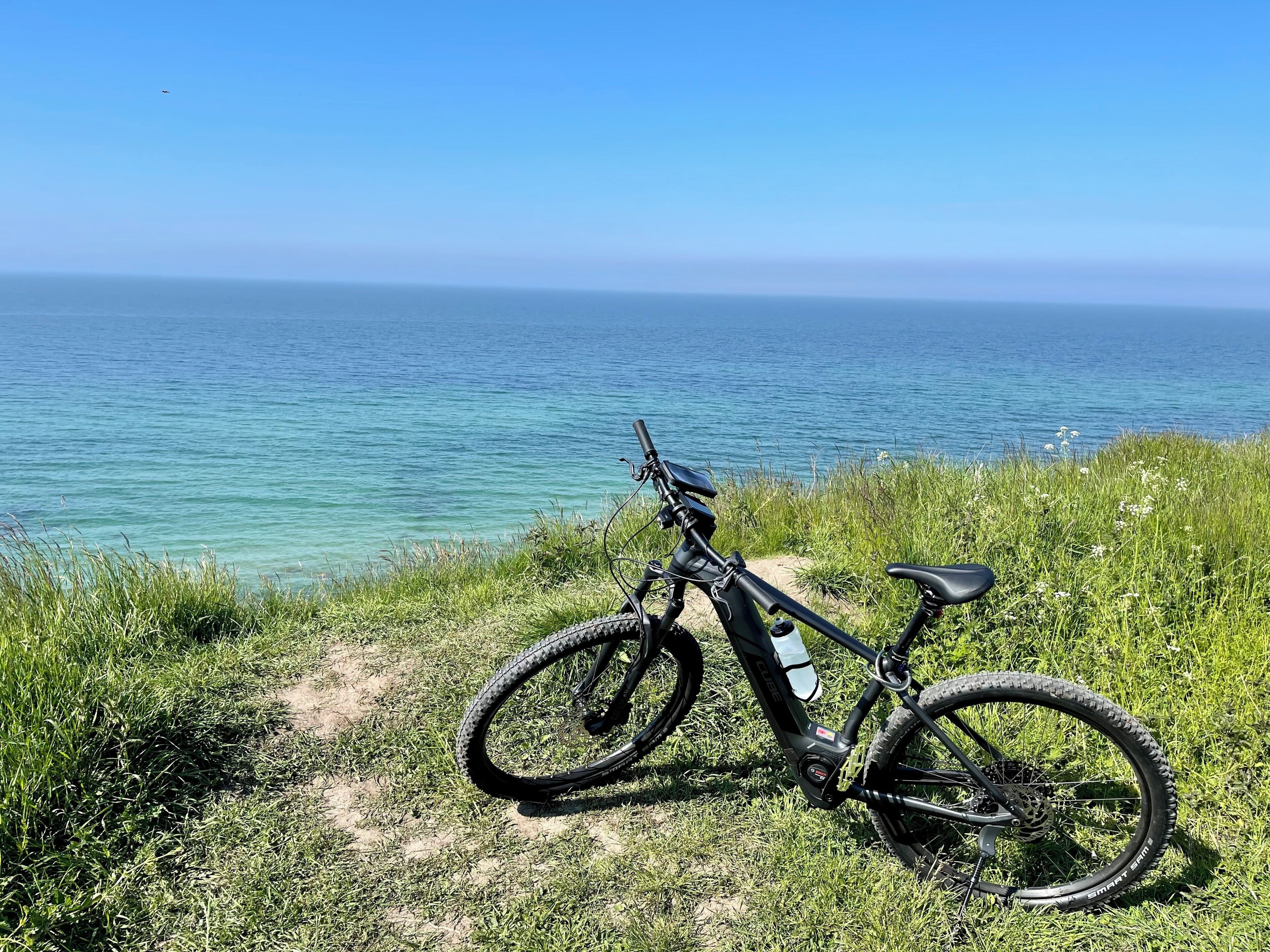 Un vélo tout-terrain est garé sur un sentier herbeux, offrant une vue sur l’océan.