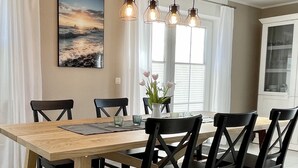 Un coin repas avec une table en bois, des chaises noires, un luminaire suspendu et un tableau au mur.