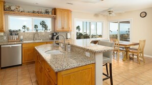 A kitchen with granite countertops, wooden cabinets, a built-in dishwasher, and a dining area with a table and chairs. - Spectacular Ocean View! (Rancho Palos Verdes)