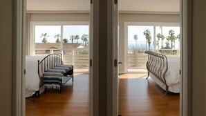 A room with a bed, a bench, and a view of palm trees and a deck outside. - Spectacular Ocean View! (Rancho Palos Verdes)