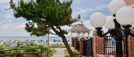 A pathway leading to a beach with umbrellas, a gazebo, and a lamp post.