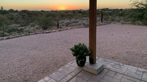 A covered patio with a gravel ground, a potted plant, and a view of a desert landscape at sunset. - 5yr old home , private, 1-BdRm home on its own 3.3 acres with city views (Tucson)