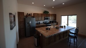 A modern kitchen with wooden cabinets, stainless steel appliances, and a large island with bar stools. - 5yr old home , private, 1-BdRm home on its own 3.3 acres with city views (Tucson)