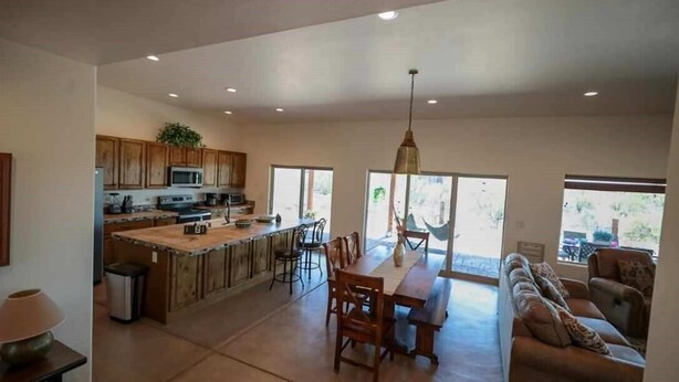 A spacious kitchen with wooden cabinets, a central island, and a dining area with a bench and chairs. - 5yr old home , private, 1-BdRm home on its own 3.3 acres with city views (Tucson)