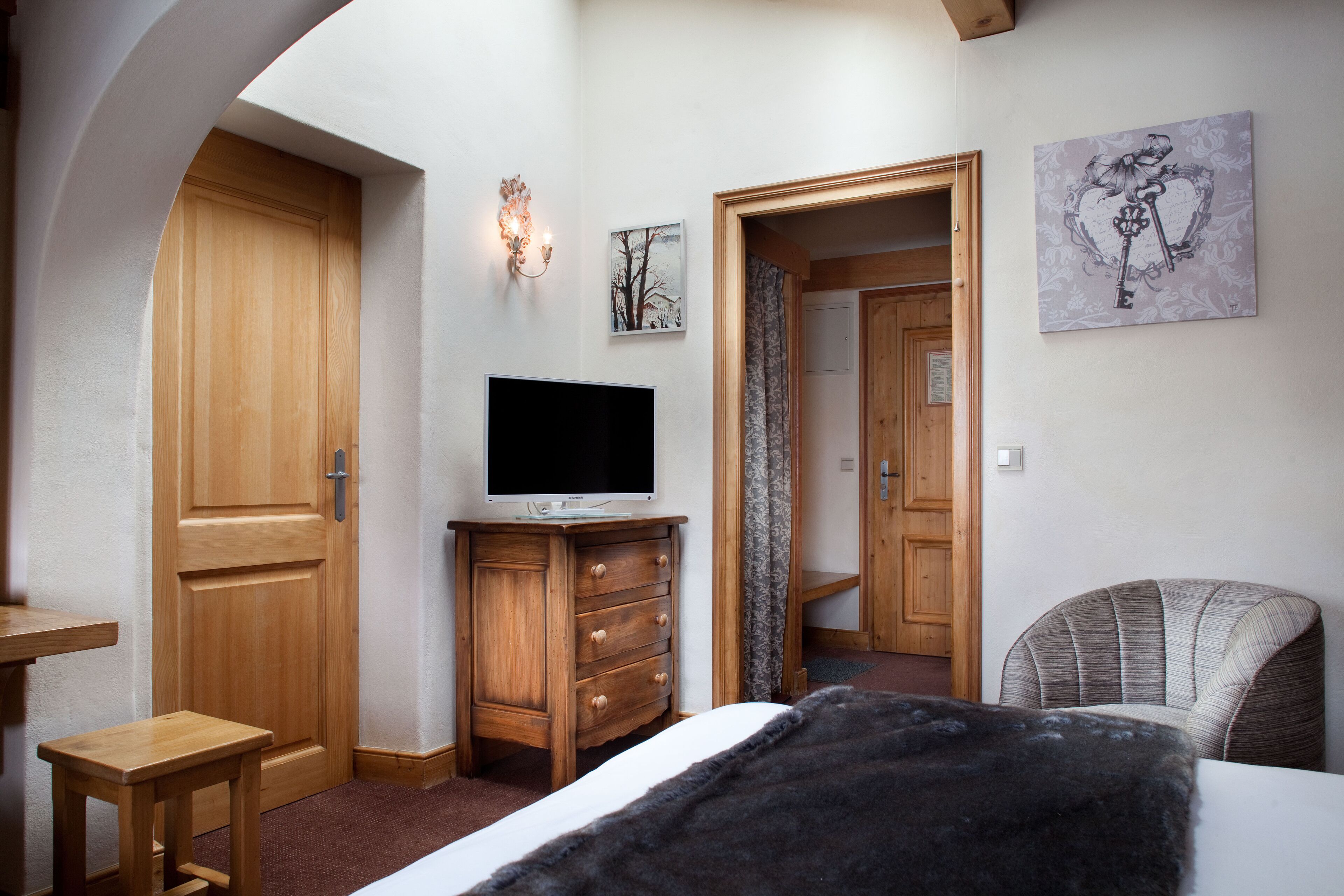 Une chambre avec une armoire en bois, un téléviseur posé sur une commode, un lit recouvert d’une couverture noire et une chaise.