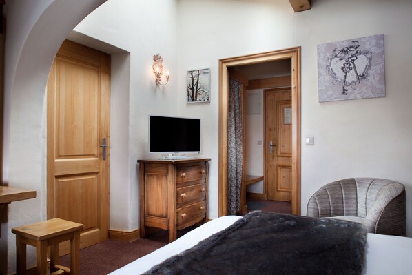 A bedroom with a wooden wardrobe, a television on a dresser, a bed with a black blanket, and a chair. - La Grange d'Arly (Megeve)
