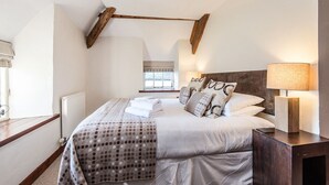 Un dormitorio con cama, almohadas, mesita de noche, lámpara y ventana.