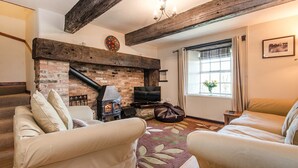 Una sala de estar acogedora con chimenea, dos sofás, un televisor y una ventana con cortinas.
