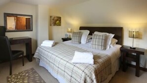 A neatly made bed with a checkered duvet and pillows, a desk with a chair, and two bedside lamps.